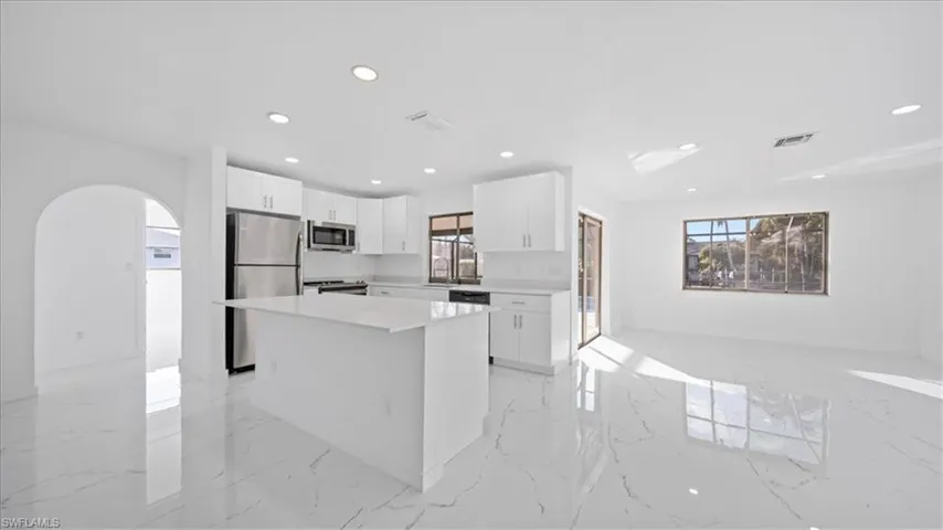Kitchen featuring arched walkways, white cabinetry, appliances with stainless steel finishes, light marble finish flooring, and a kitchen island