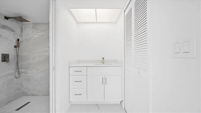 Bathroom featuring vanity, a marble finish shower, a closet, and light marble finish flooring
