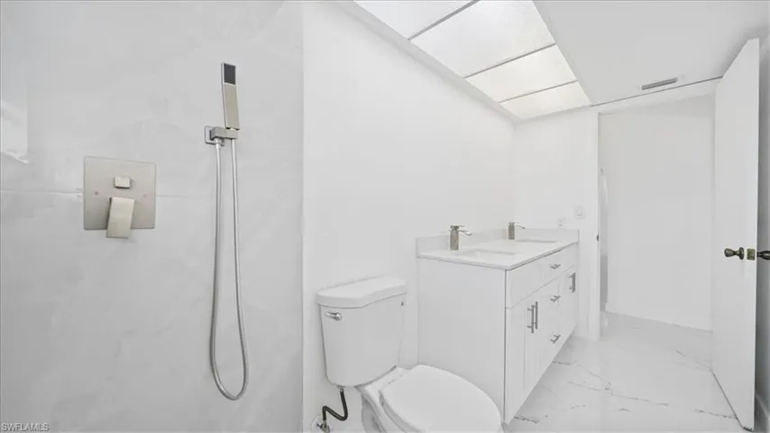Bathroom featuring light marble finish flooring, double vanity, and a marble finish shower