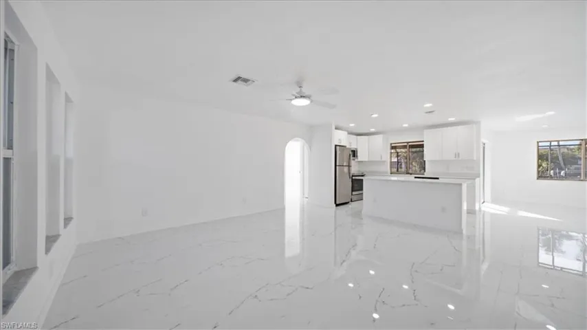 Unfurnished living room featuring recessed lighting, arched walkways, light marble finish flooring, and a ceiling fan