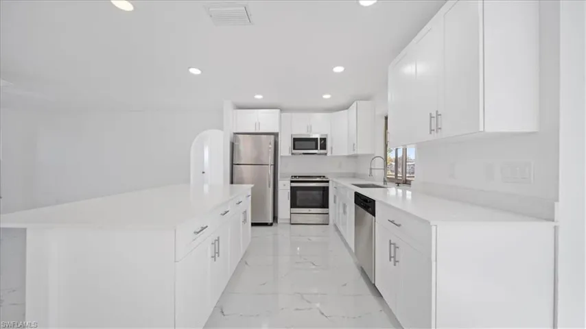 Kitchen featuring appliances with stainless steel finishes, white cabinetry, recessed lighting, a kitchen island, and light marble finish floors