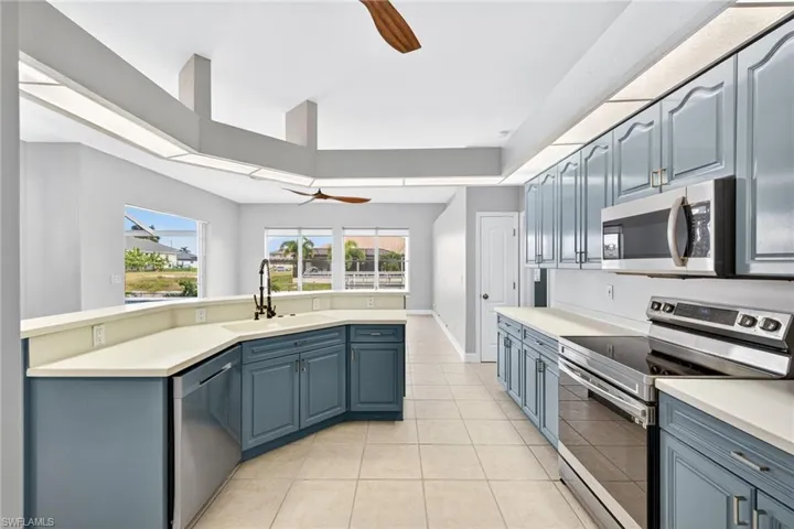 Kitchen featuring stainless steel appliances, blue cabinetry, a ceiling fan, light countertops, and light tile patterned floors