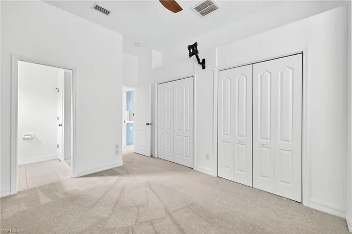Unfurnished bedroom featuring multiple closets, light carpet, and ceiling fan
