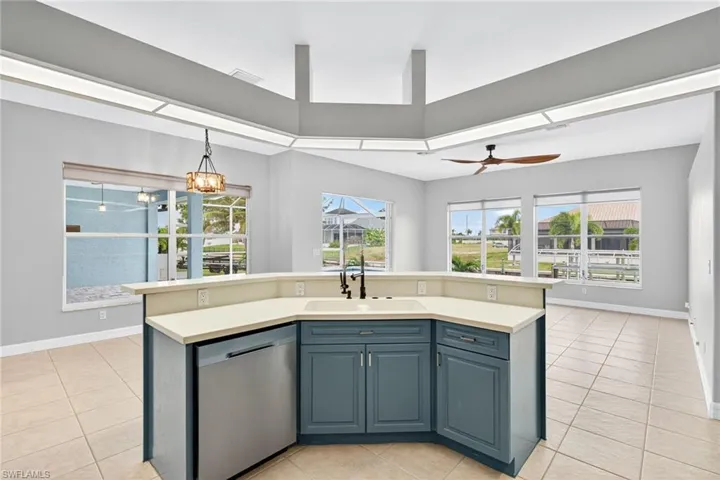 Kitchen featuring an island with sink, light tile patterned floors, stainless steel dishwasher, light countertops, and plenty of natural light