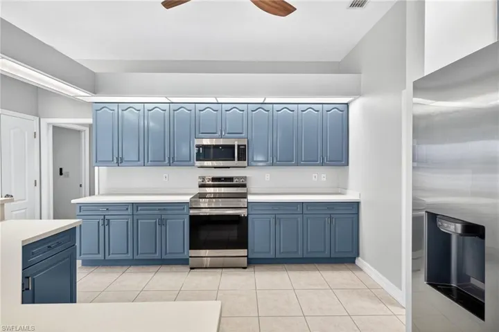 Kitchen with blue cabinetry, appliances with stainless steel finishes, light countertops, light tile patterned floors, and ceiling fan