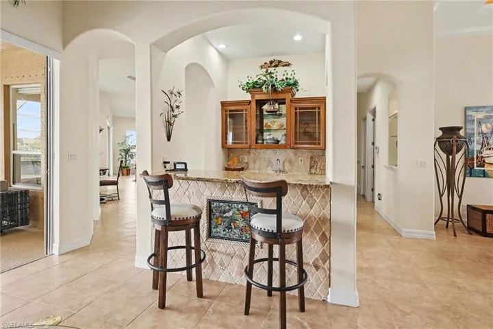 Indoor bar with glass fronted cabinets, wood finish cabinets, decorative backsplash, light stone counters, and arched walkways