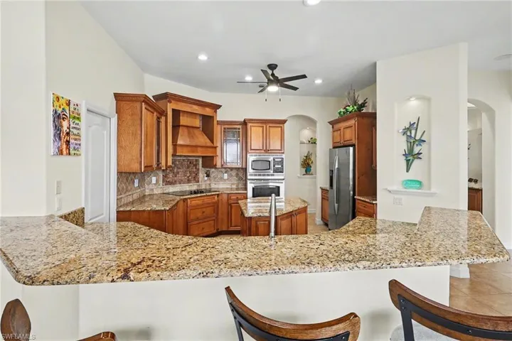 Kitchen with arched walkways, wood finish cabinetry, a breakfast bar, a peninsula, and decorative backsplash