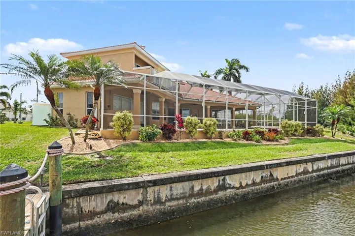 Back of house with a water view, a sunroom, a lanai, and a lawn