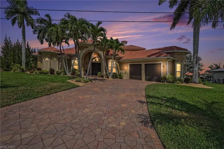 Mediterranean / spanish-style house with a yard, stucco siding, an attached garage, a tiled roof, and decorative driveway