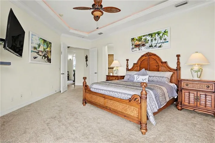 Bedroom with ornamental molding, light colored carpet, a ceiling fan, and a raised ceiling