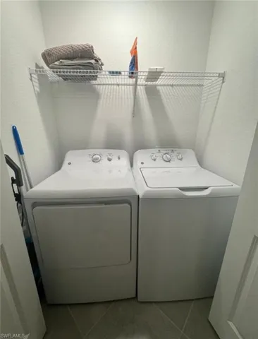 Laundry area with tile patterned floors, separate washer and dryer, and a textured wall