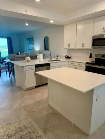 Kitchen with stainless steel appliances, a peninsula, white cabinetry, a center island, and light stone counters