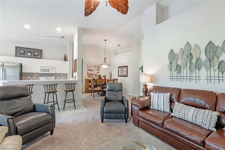 Living room with light colored carpet, high vaulted ceiling, ceiling fan, and light tile patterned floors