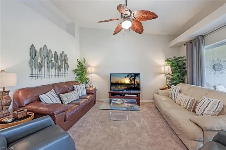 Living area featuring a ceiling fan, carpet flooring, and lofted ceiling