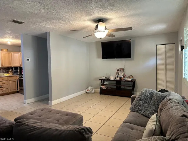 Living room featuring a textured ceiling, ceiling fan, and light tile patterned floors