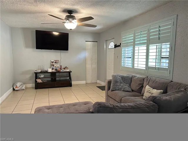 Living room featuring a textured ceiling, light tile patterned floors, and ceiling fan