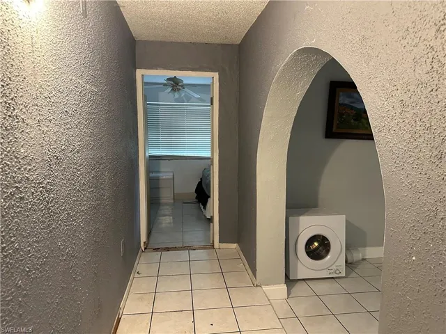 Hall with a textured ceiling, washer / dryer, and light tile patterned floors