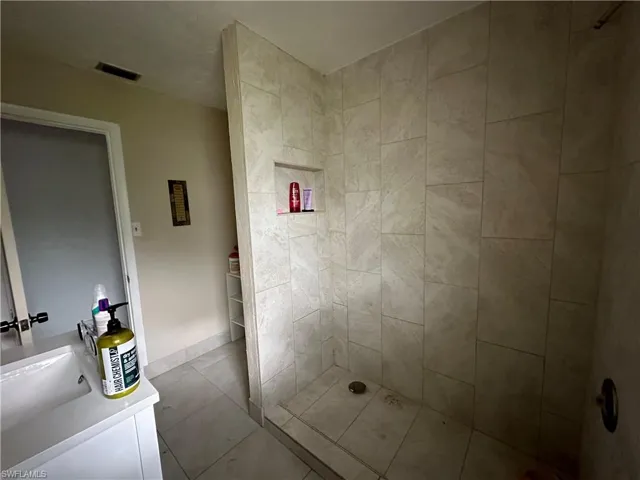 Bathroom with vanity, tiled shower, and tile patterned flooring