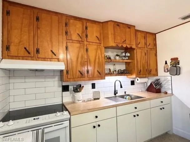 Kitchen featuring white electric stove, open shelves, under cabinet range hood, backsplash, and brown cabinets