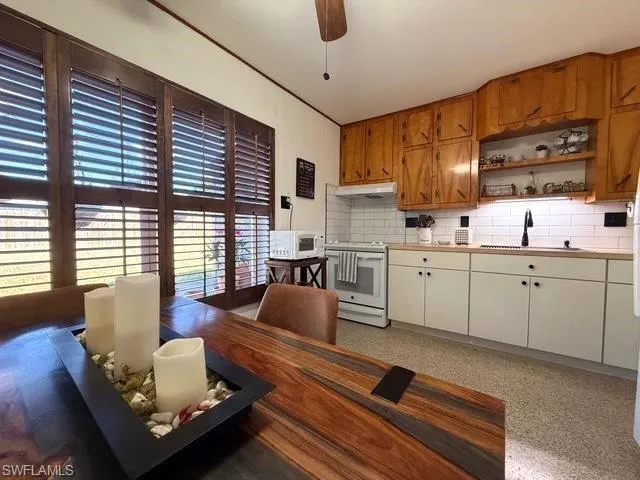 Kitchen with a ceiling fan, white appliances, decorative backsplash, dark speckled floor, and open shelves
