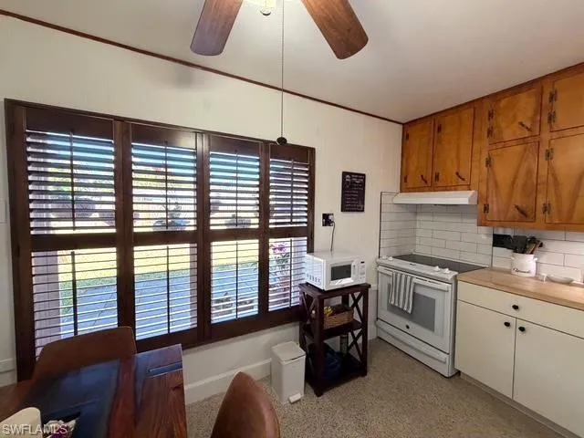 Kitchen with decorative backsplash, white appliances, a ceiling fan, butcher block countertops, and under cabinet range hood