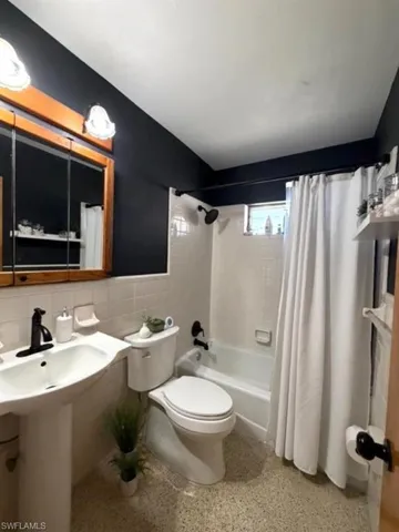 Full bathroom featuring tile walls, shower / tub combo with curtain, dark aggregate flooring, and wainscoting