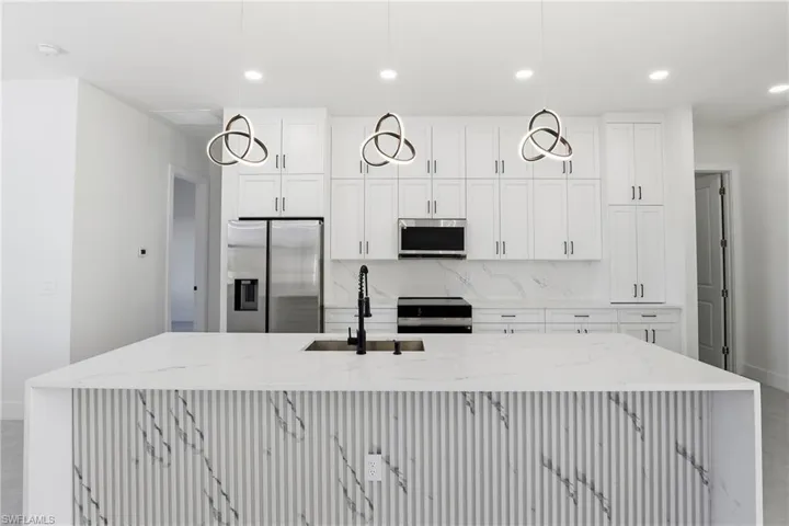 Kitchen featuring light stone counters, stainless steel appliances, decorative backsplash, white cabinets, and recessed lighting