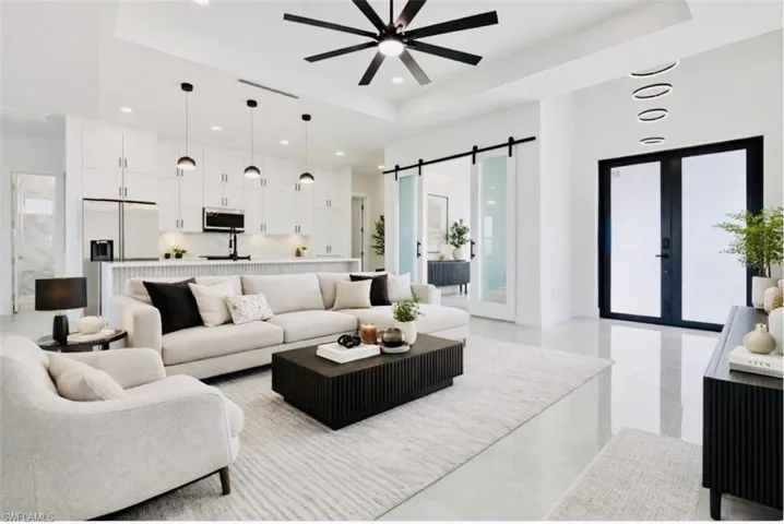 Living area featuring a barn door, a raised ceiling, a ceiling fan, french doors, and recessed lighting. Digitally Staged.