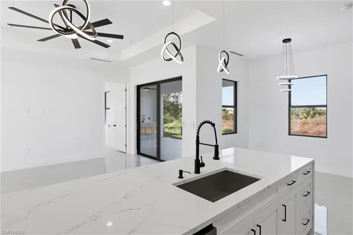 Kitchen with decorative light fixtures, light stone countertops, white cabinets, plenty of natural light, and recessed lighting