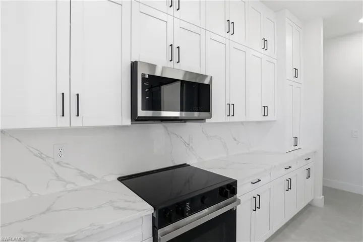 Kitchen featuring range with electric cooktop, stainless steel microwave, light stone countertops, and white cabinetry