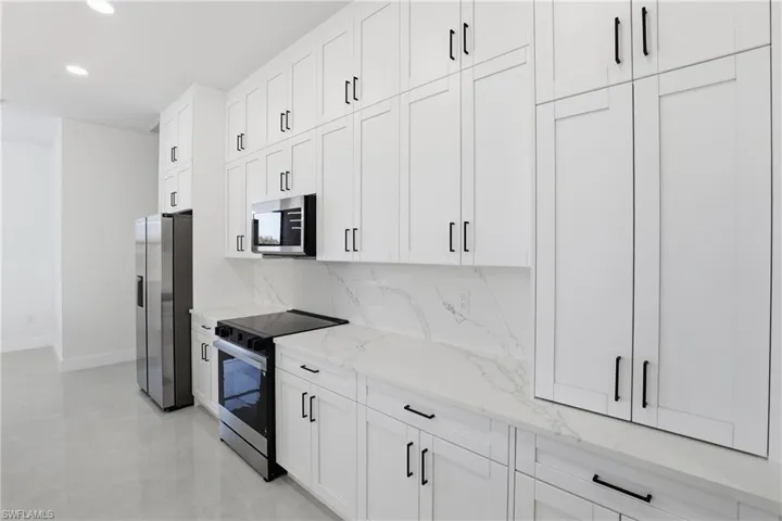 Kitchen featuring stainless steel appliances, white cabinets, light stone countertops, recessed lighting, and tasteful backsplash