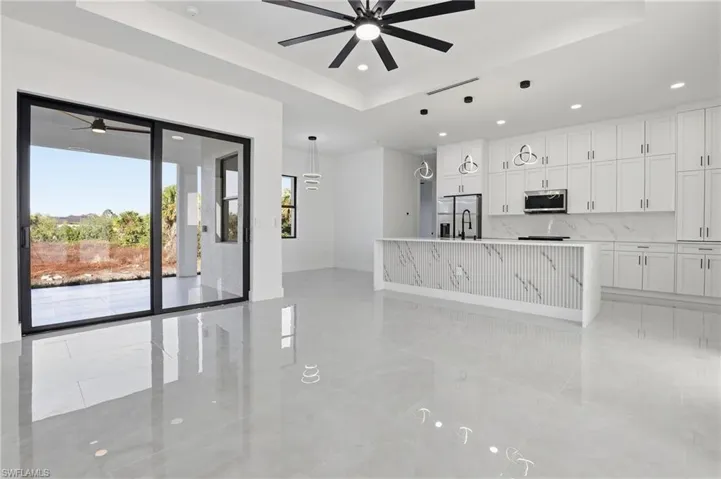 Kitchen featuring a raised ceiling, a ceiling fan, an island with sink, white cabinetry, and recessed lighting