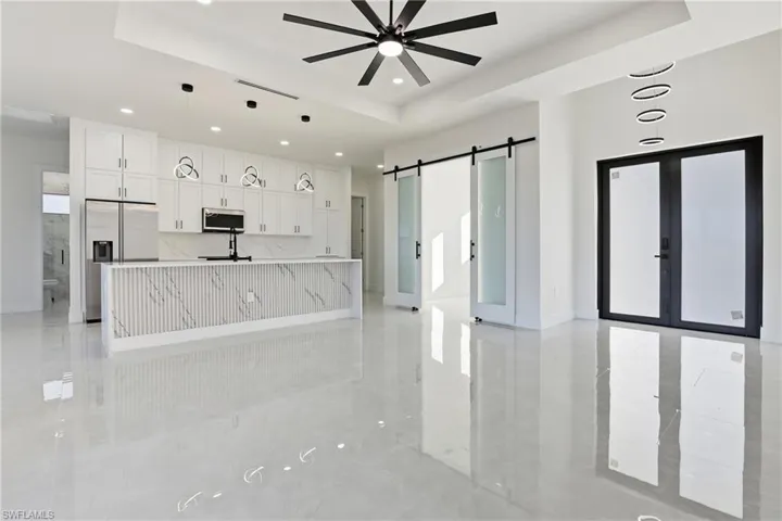 Kitchen featuring white cabinets, a raised ceiling, appliances with stainless steel finishes, an island with sink, and recessed lighting