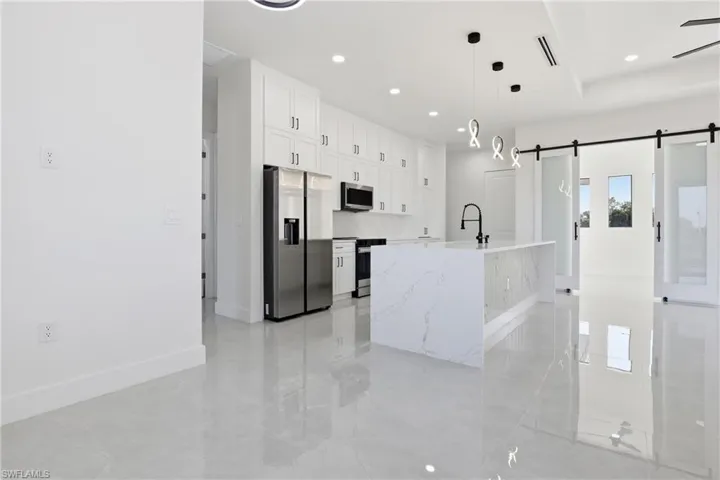 Kitchen with stainless steel appliances, white cabinetry, a barn door, decorative light fixtures, and light stone counters