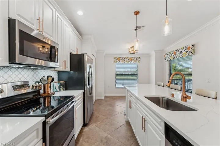Kitchen featuring appliances with stainless steel finishes, sink, white cabinets, hanging light fixtures, and crown molding