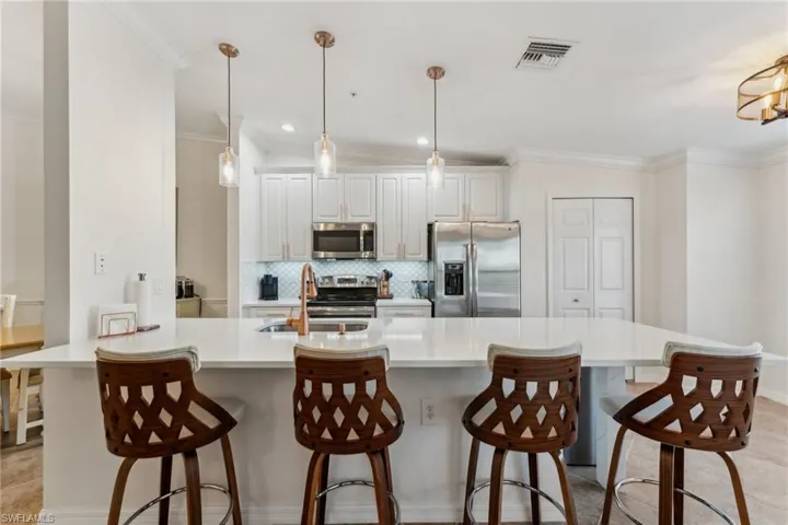 Kitchen with sink, white cabinetry, appliances with stainless steel finishes, pendant lighting, and backsplash