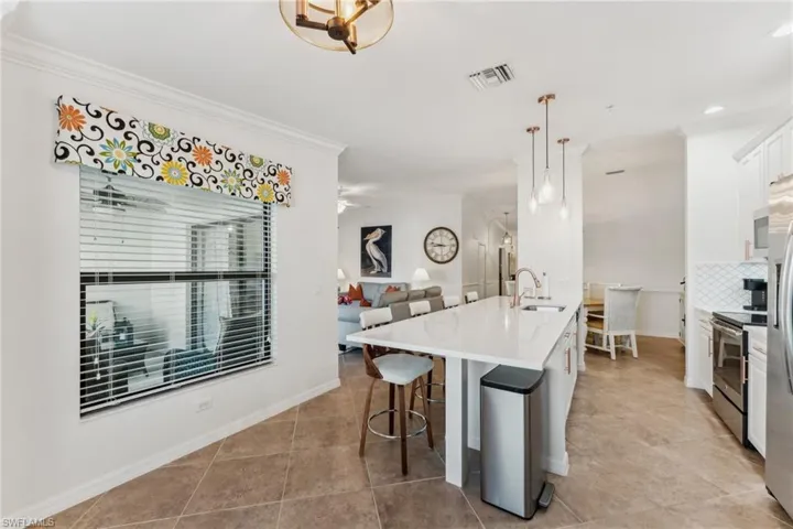Kitchen with a breakfast bar, white cabinetry, an island with sink, sink, and hanging light fixtures