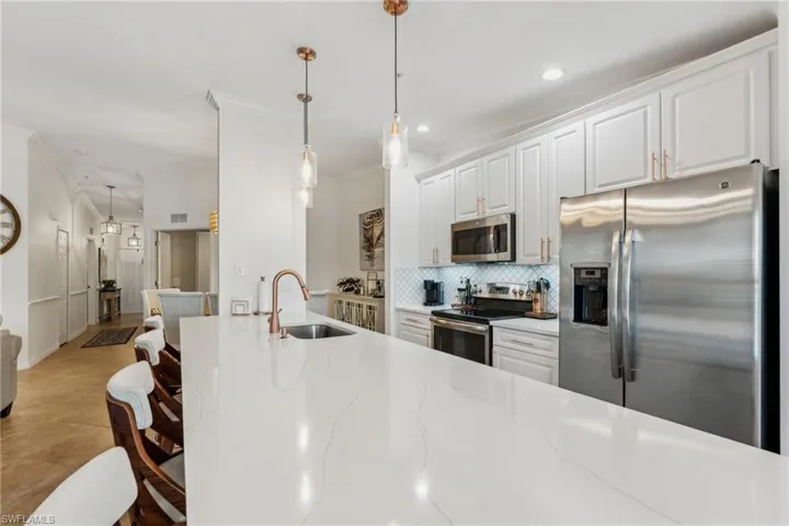 Kitchen featuring stainless steel appliances, white cabinetry, light stone countertops, and sink