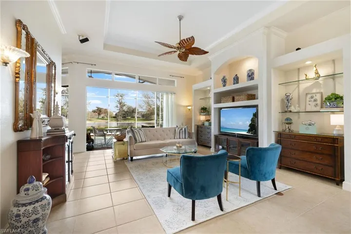 Living room with light tile patterned floors, built in shelves, a raised ceiling, and crown molding