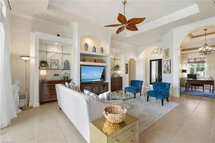 Living room featuring built in features, arched walkways, a raised ceiling, and light tile patterned flooring