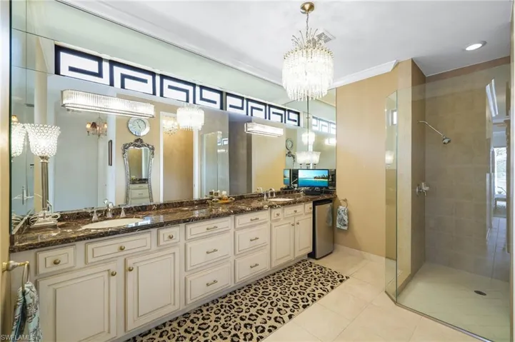 Full bathroom with a notable chandelier, dual vanities and a tiled shower