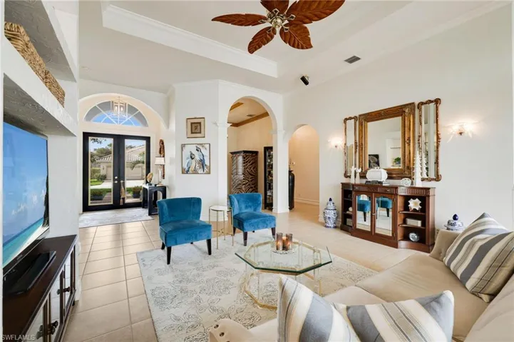 Living area featuring arched walkways, light tile patterned floors, a tray ceiling, and decorative columns