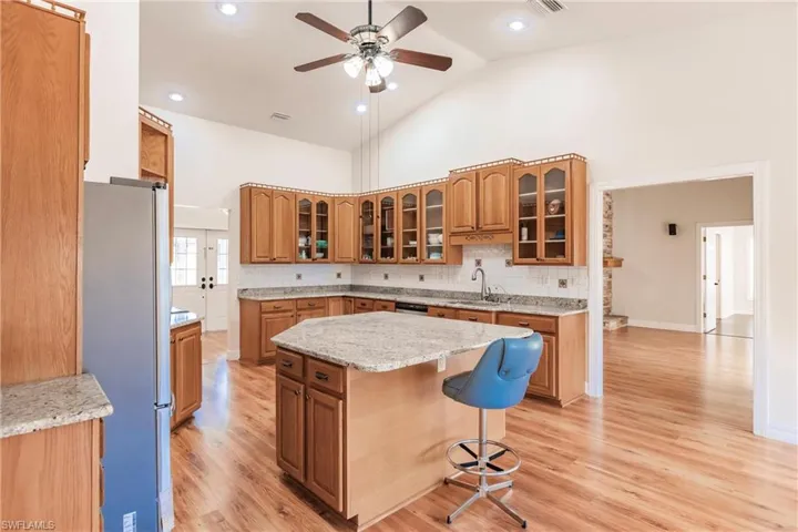 Kitchen featuring stainless steel fridge, decorative backsplash, a kitchen island, high vaulted ceiling, and sink