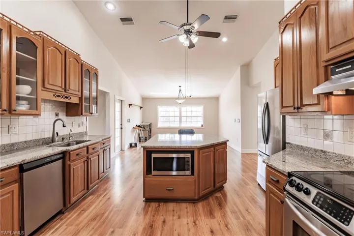 Kitchen featuring vaulted ceiling, appliances with stainless steel finishes, a center island, light stone countertops, and sink