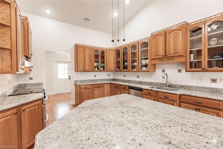 Kitchen featuring stainless steel appliances, high vaulted ceiling, light stone countertops, and sink