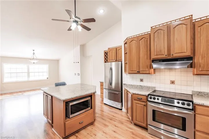 Kitchen featuring stainless steel appliances, light stone counters, decorative backsplash, light hardwood / wood-style flooring, and lofted ceiling