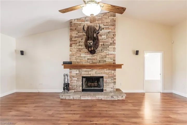 Unfurnished living room featuring ceiling fan, a stone fireplace, vaulted ceiling, and wood-type flooring