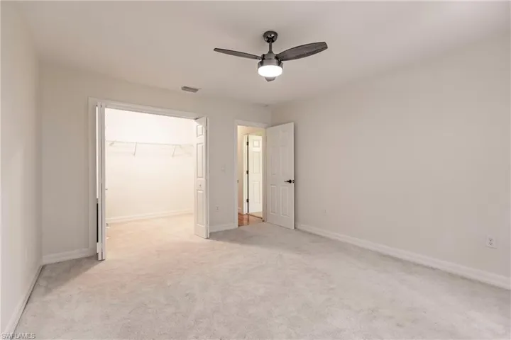 Unfurnished bedroom with ceiling fan, a walk in closet, a closet, and light colored carpet