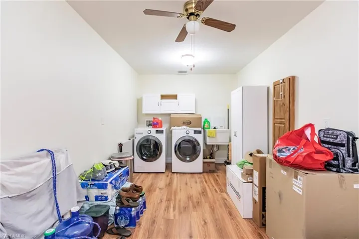 Clothes washing area with sink, cabinets, ceiling fan, light hardwood / wood-style floors, and washing machine and dryer