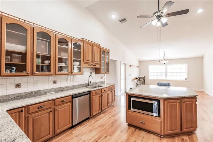 Kitchen with stainless steel appliances, light stone counters, decorative backsplash, and hanging light fixtures